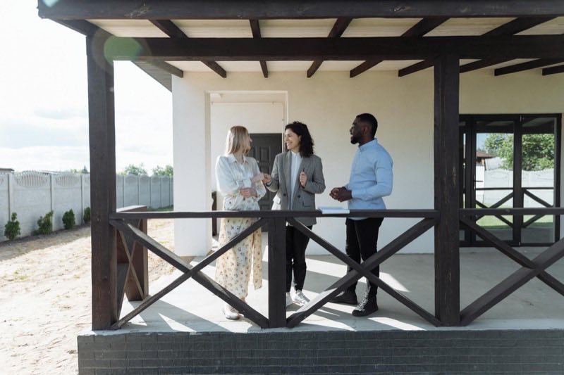 Three people talking on the covered porch of a newly built house